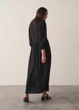 Back view of woman wearing black full length maxi dress with puffed 3/4 length sleeves, with black sandals