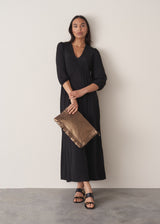 Woman wearing black full length maxi dress with puffed 3/4 length sleeves with gold clutch bag and black leather sandals