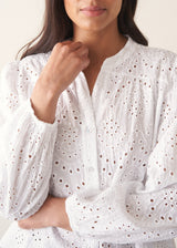 Woman wearing white broderie anglaise  long sleeve top and blue linen trousers
