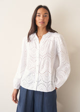 Woman wearing white broderie anglaise  long sleeve top and blue linen trousers