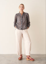 A woman wearing a dark blue long-sleeve blouse with a brown and rust-colored paisley print pattern and light trousers.