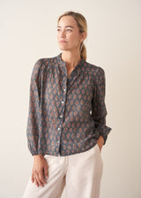 A woman wearing a dark blue long-sleeve blouse with a brown and rust-colored paisley print pattern and light trousers.