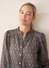 A woman wearing a dark blue long-sleeve blouse with a brown and rust-colored paisley print pattern and light trousers.