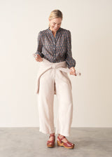 A woman wearing a dark blue long-sleeve blouse with a brown and rust-colored paisley print pattern and light trousers.