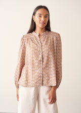 A woman wearing a long-sleeve button-up shirt with a small beige and brown floral pattern.
