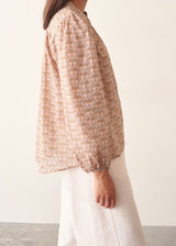 A woman wearing a long-sleeve button-up shirt with a small beige and brown floral pattern.