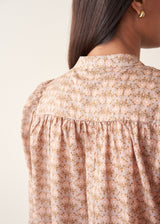 A woman wearing a long-sleeve button-up shirt with a small beige and brown floral pattern.