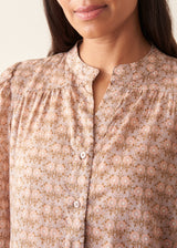 A woman wearing a long-sleeve button-up shirt with a small beige and brown floral pattern.