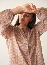 A woman wearing a long-sleeve button-up shirt with a small beige and brown floral pattern.