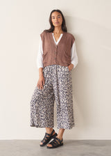 Woman wearing brown knitted waistcoat, a white cotton top and leopard print trousers