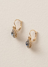 Side view of a pair of drop earrings with diamante crystals surrounding a deep navy blue central crystal, on a beige backdrop