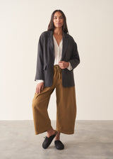A woman wearing a dark charcoal textured blazer with olive barrel leg trousers and a white blouse