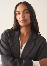 A woman wearing a dark charcoal textured blazer with olive barrel leg trousers and a white blouse