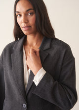A woman wearing a dark charcoal textured blazer with olive barrel leg trousers and a white blouse