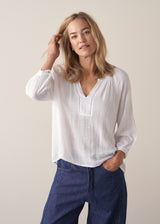 Woman wearing a white lightweight cotton blouse with long sleeves and blue barrel leg jeans