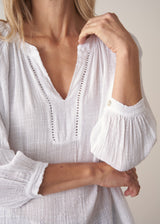 Woman wearing a white lightweight cotton blouse with long sleeves and blue barrel leg jeans