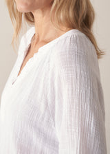 Woman wearing a white lightweight cotton blouse with long sleeves and blue barrel leg jeans