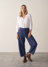 Woman wearing a white lightweight cotton blouse with long sleeves and blue barrel leg jeans