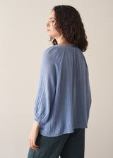 Woman wearing cornflower blue cotton blouse with dark teal linen trousers