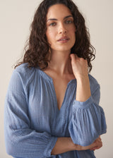 Woman wearing cornflower blue cotton blouse with dark teal linen trousers
