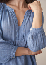Woman wearing cornflower blue cotton blouse with dark teal linen trousers