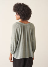 Woman wearing pale green cotton top with black linen trousers. 