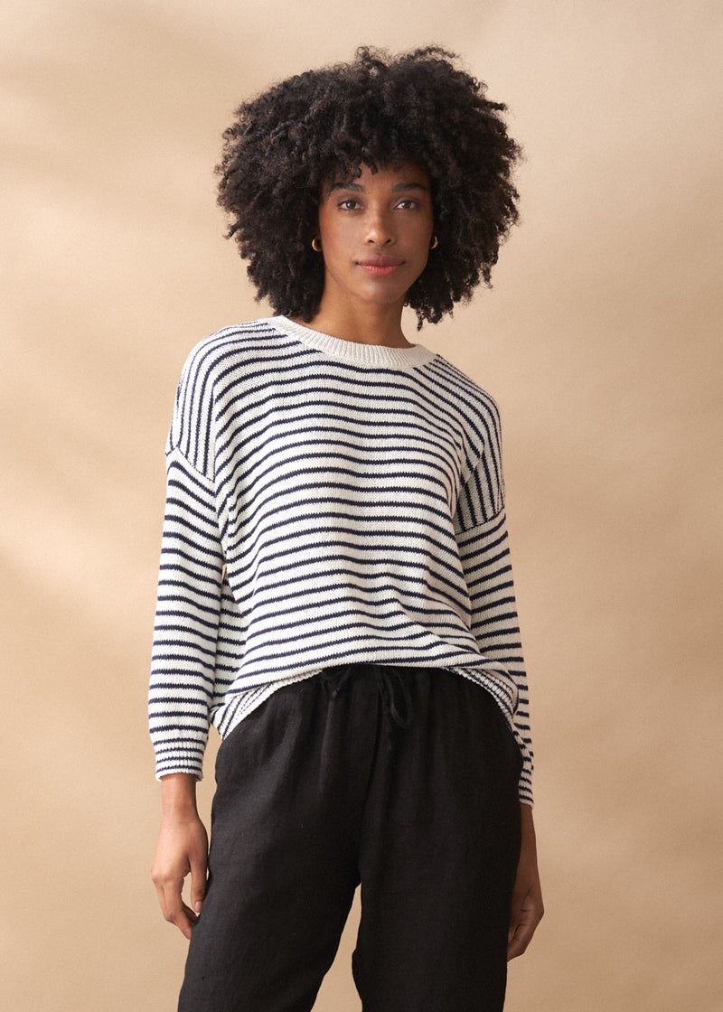 Woman wearing striped light knit sweater with crew neck, and black trousers
