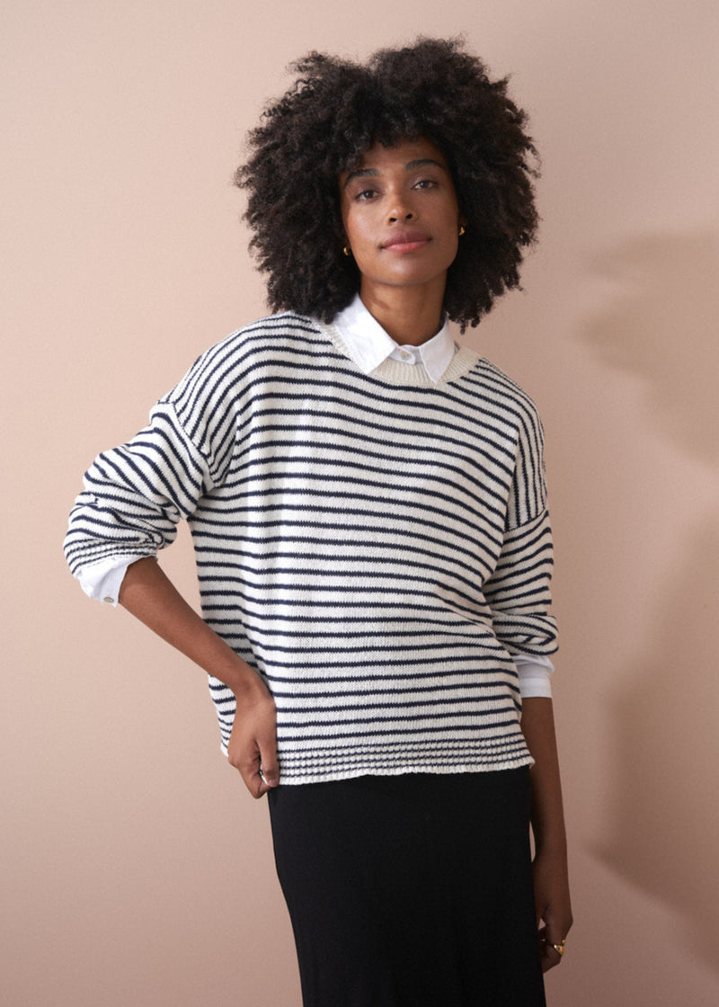 Woman wearing light knit stripe sweater with crew neck and black satin skirt