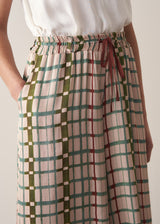 Woman wearing silk blend wide-leg trousers in check print with a sleeveless satin top against a beige background