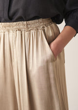 Woman wearing taupe satin wide leg trousers with a black shirt and black sandals
