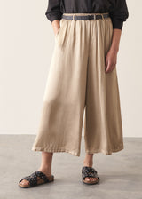 Woman wearing taupe satin wide leg trousers with a black shirt and black sandals