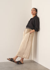 Woman wearing taupe satin wide leg trousers with a black shirt and black sandals