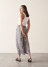A woman wearing wide-leg leopard print trousers and a white vest top. 