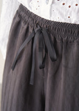 Woman wearing charcoal black stripe wide leg cropped trousers with a white broderie shirt.