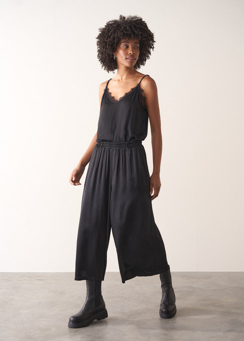 Woman wearing black satin wide leg cropped trousers against a plain background