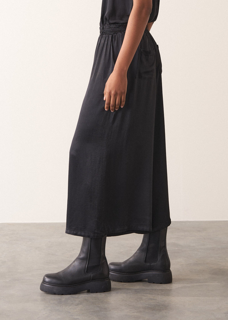 Woman wearing black satin wide leg cropped trousers against a plain background