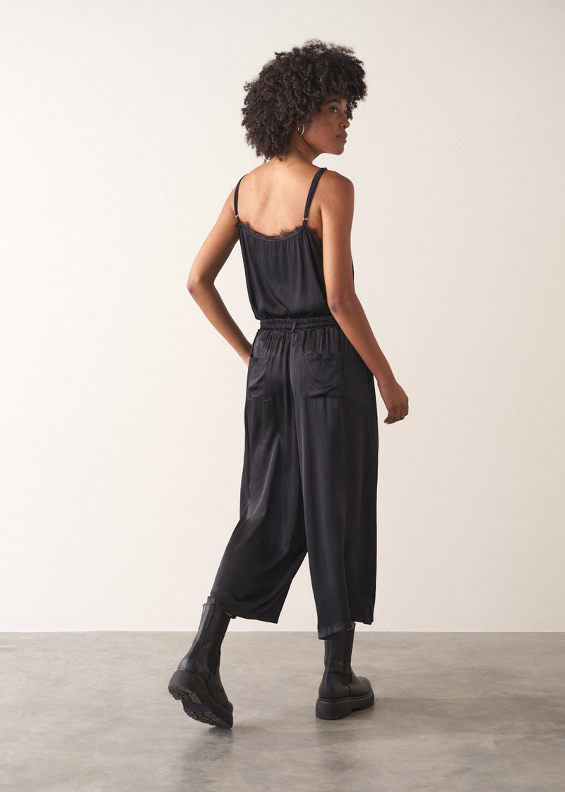 Woman wearing black satin wide leg cropped trousers against a plain background