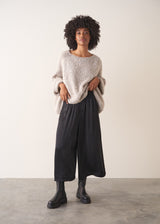 Woman wearing black satin wide leg cropped trousers against a plain background