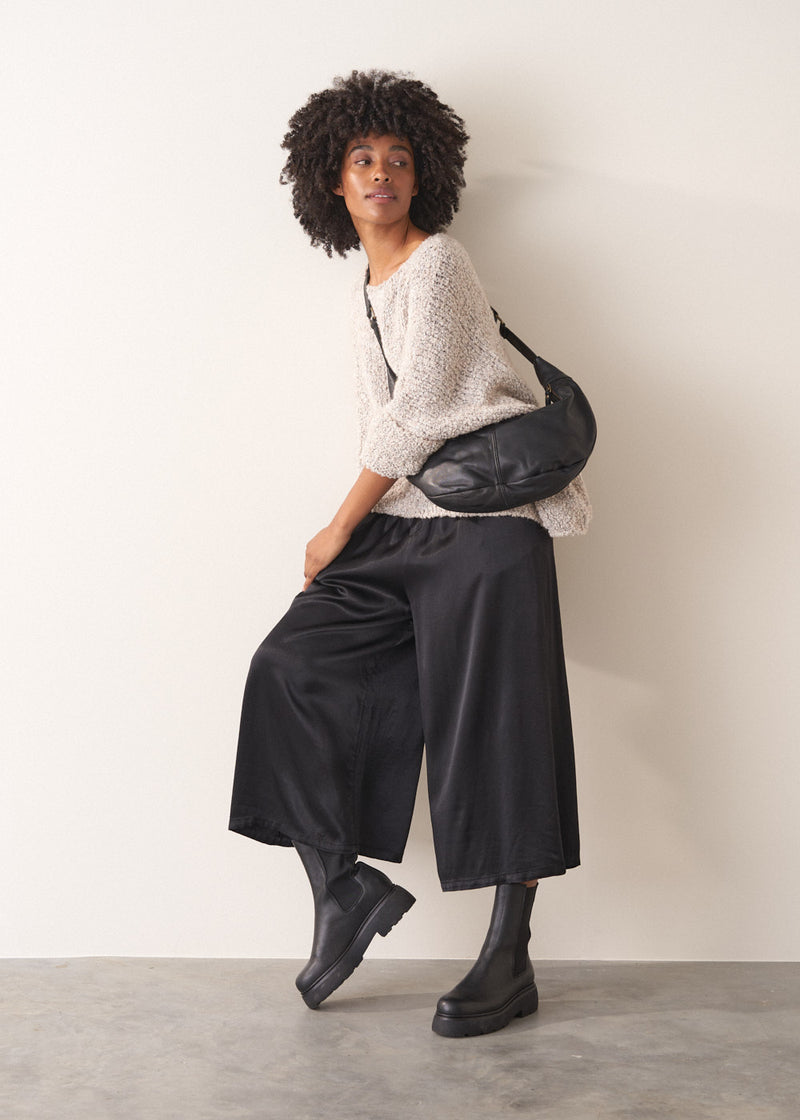 Woman wearing black satin wide leg cropped trousers against a plain background