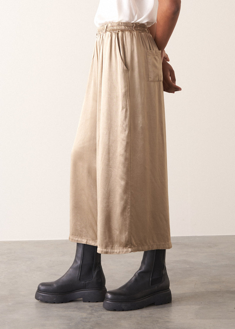 Woman wearing a white sleeveless top and champagne satin wide-leg trousers against a plain background