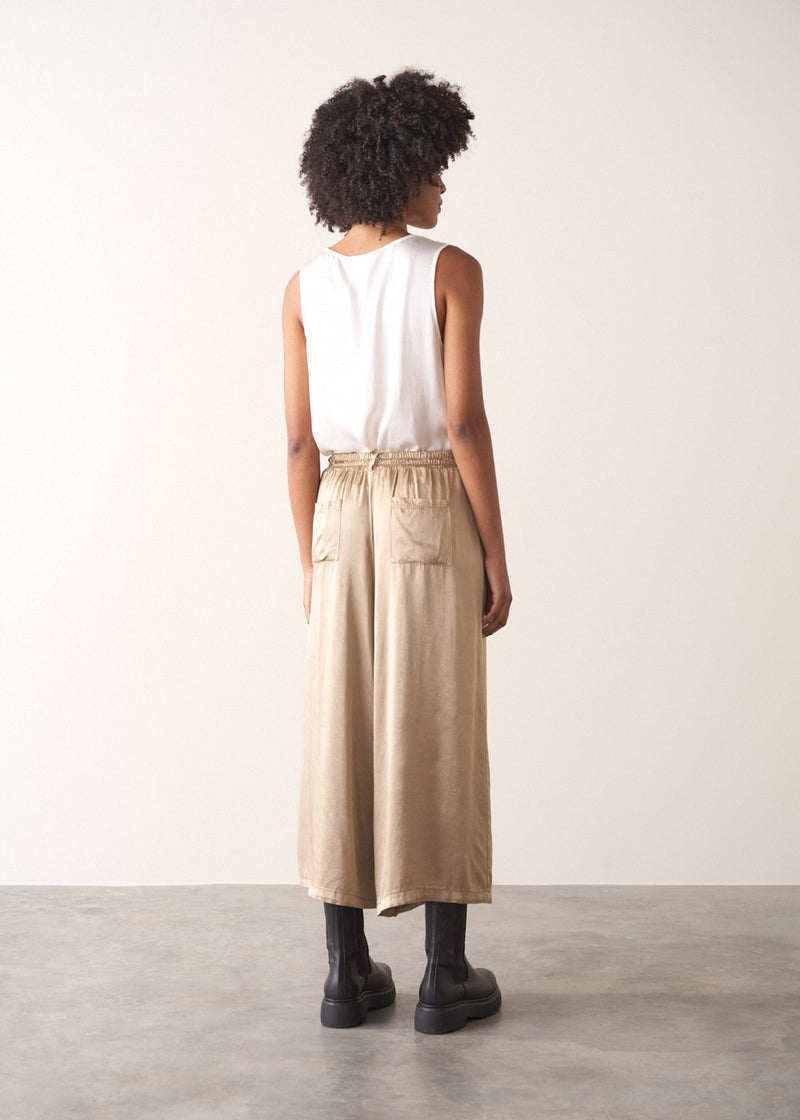 Woman wearing a white sleeveless top and champagne satin wide-leg trousers against a plain background