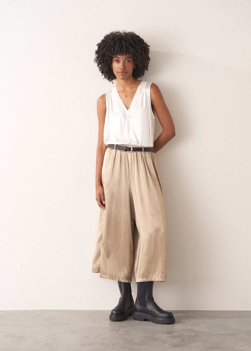 Woman wearing a white sleeveless top and champagne satin wide-leg trousers against a plain background