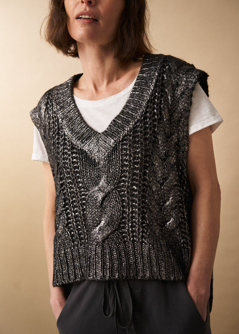 Woman wears a dark grey silver metallic cable knit vest, white short sleeve t-shirt and black jersey drawstring trousers