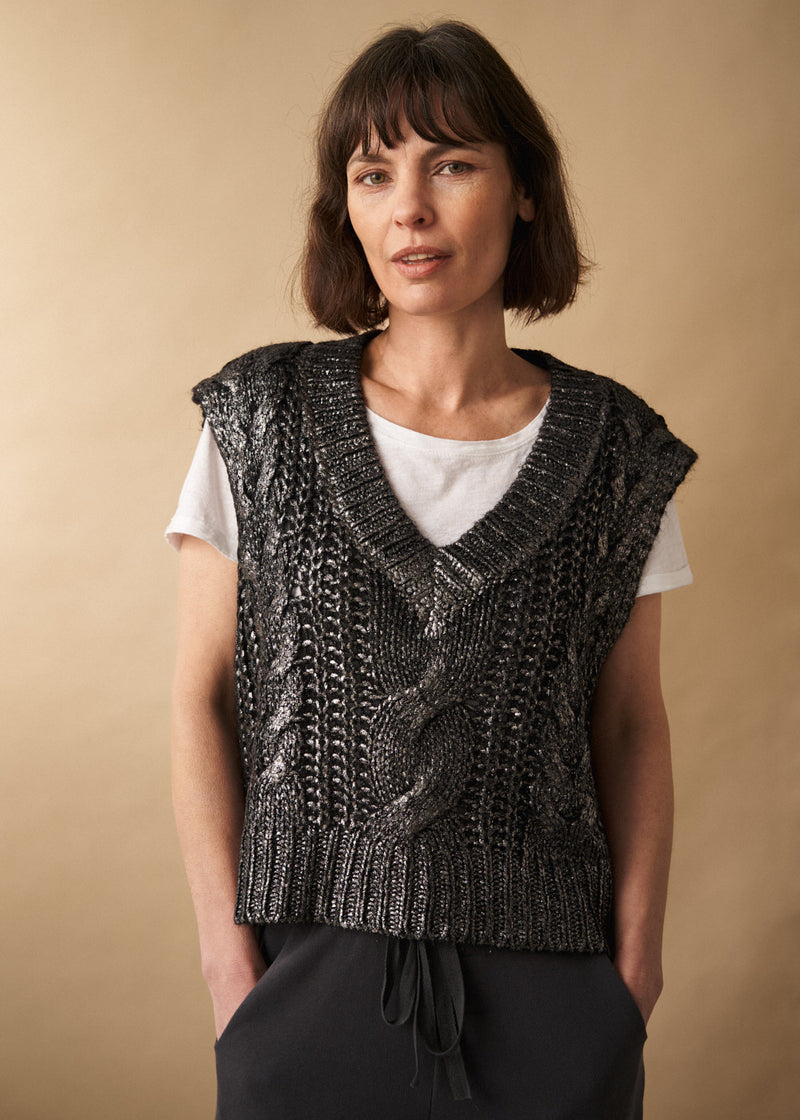 woman wears a grey silver metallic cable knit vest with short sleeve t-shirt and black jersey trousers