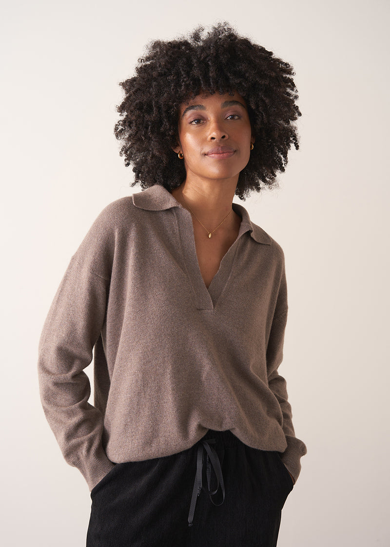Woman wearing a light brown long-sleeve polo neck sweater and black drawstring trousers against a plain background