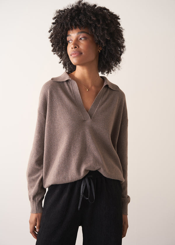 Woman wearing a light brown long-sleeve polo neck sweater and black drawstring trousers against a plain background