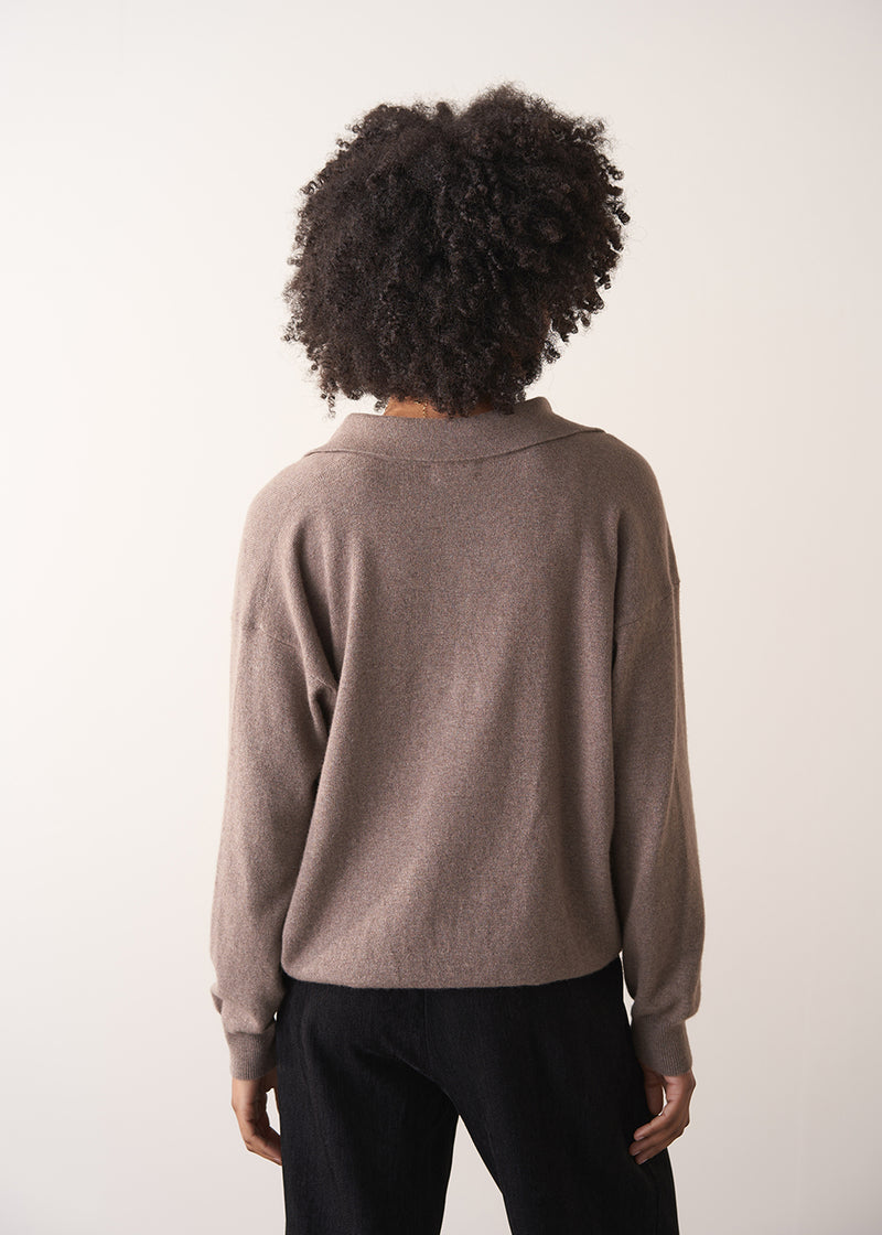 Woman wearing a light brown long-sleeve polo neck sweater and black drawstring trousers against a plain background