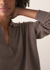 Woman wearing a light brown long-sleeve polo neck sweater and black drawstring trousers against a plain background