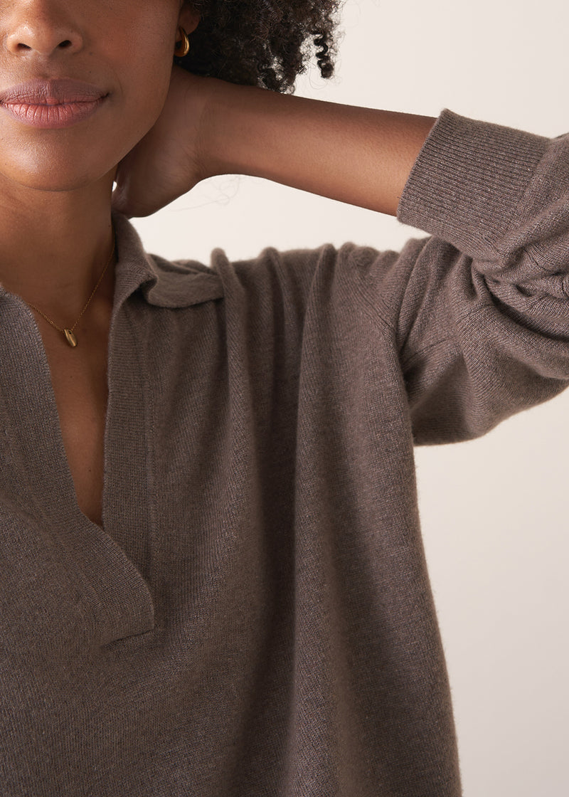 Woman wearing a light brown long-sleeve polo neck sweater and black drawstring trousers against a plain background