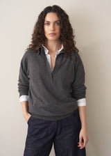 Woman wearing a dark grey polo neck collared jumper and denim wide leg jeans against a beige background